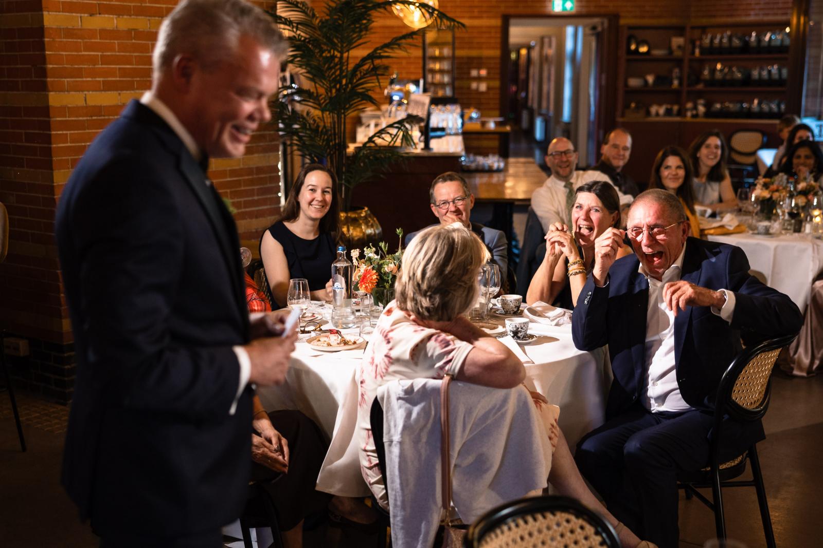 Gasten schieten in de lach en laten een traan tijdens de speech van bruidegom Mike tijdens het huwelijksdiner.