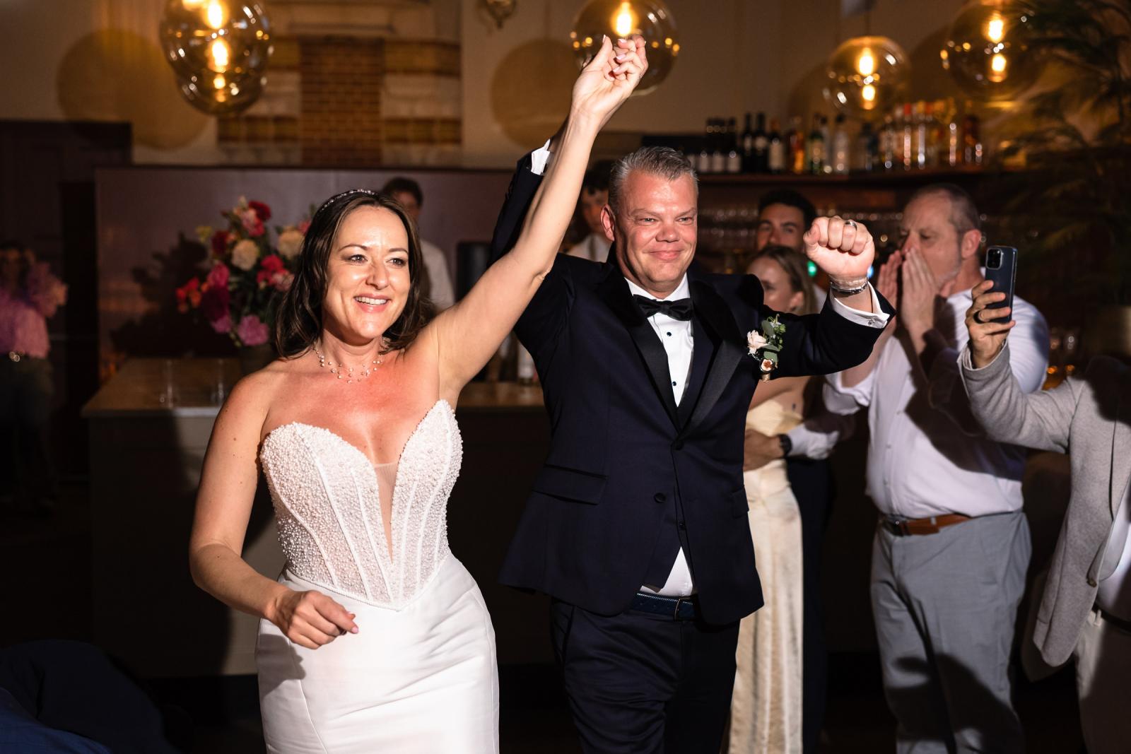 Feestelijke binnenkomst van bruidspaar Mike en Nadine met opgeheven handen bij de opening van het feest.