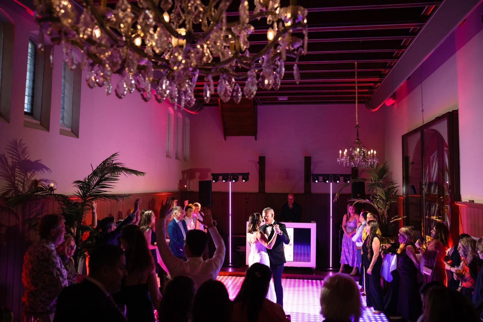 Overzichtsfoto van de sfeervol verlichte feestzaal tijdens de intieme openingsdans van het bruidspaar.