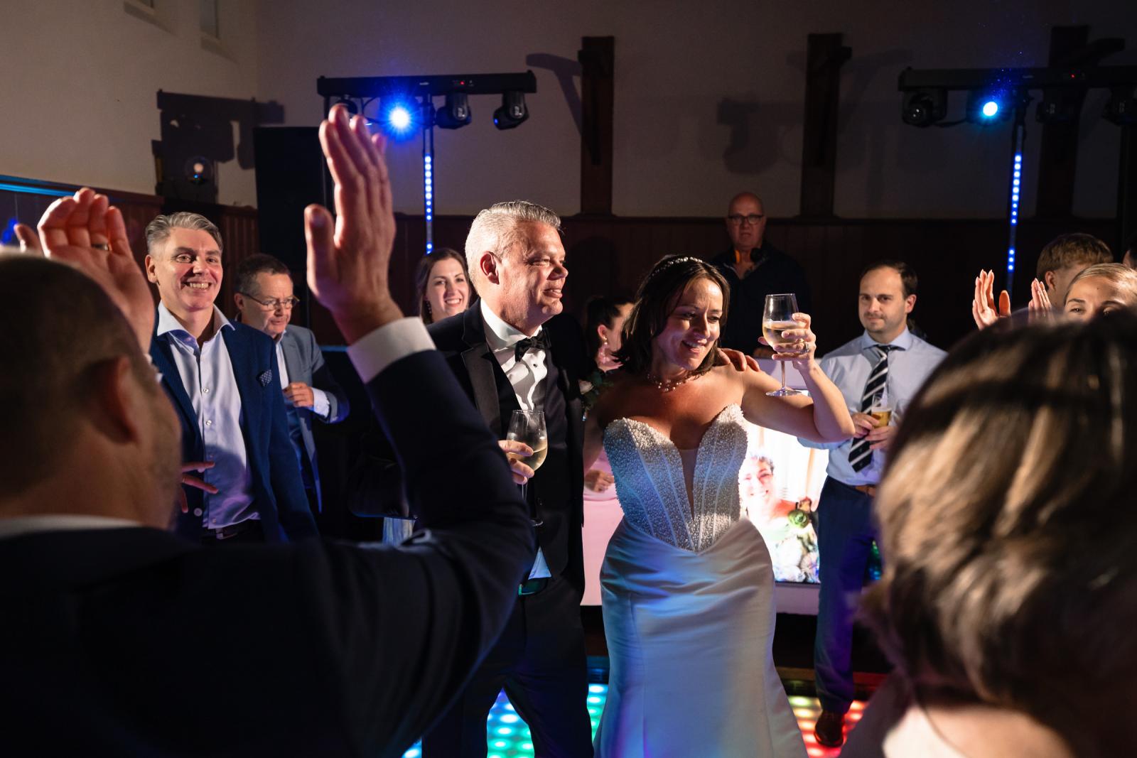 Bruid Nadine en bruidegom Mike proosten stralend op de dansvloer te midden van feestende gasten.