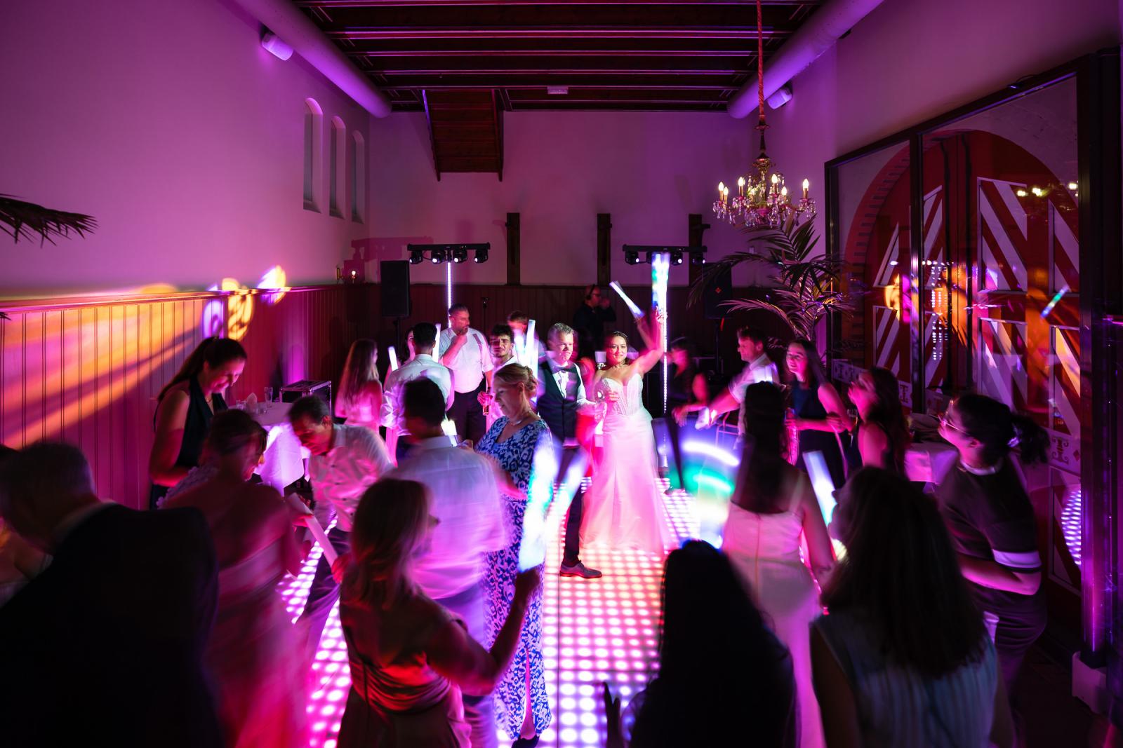 Bruisend overzicht van een volle dansvloer waar het bruidspaar en gasten feesten met gekleurde lichtstaven.
