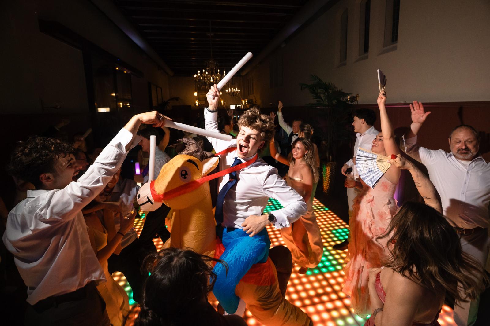 Een bruiloftsgast feest uitgelaten op het opblaasbare paard te midden van juichende gasten met lichtstaven.