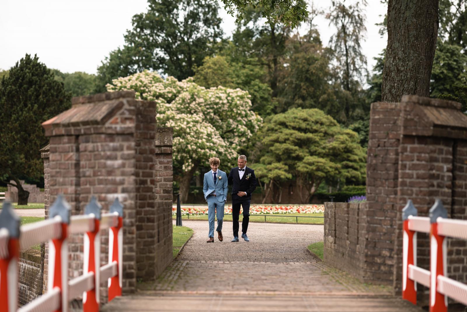 Bruidegom Mike en zijn zoon lopen samen over de brug in de tuinen van Kasteel de Haar