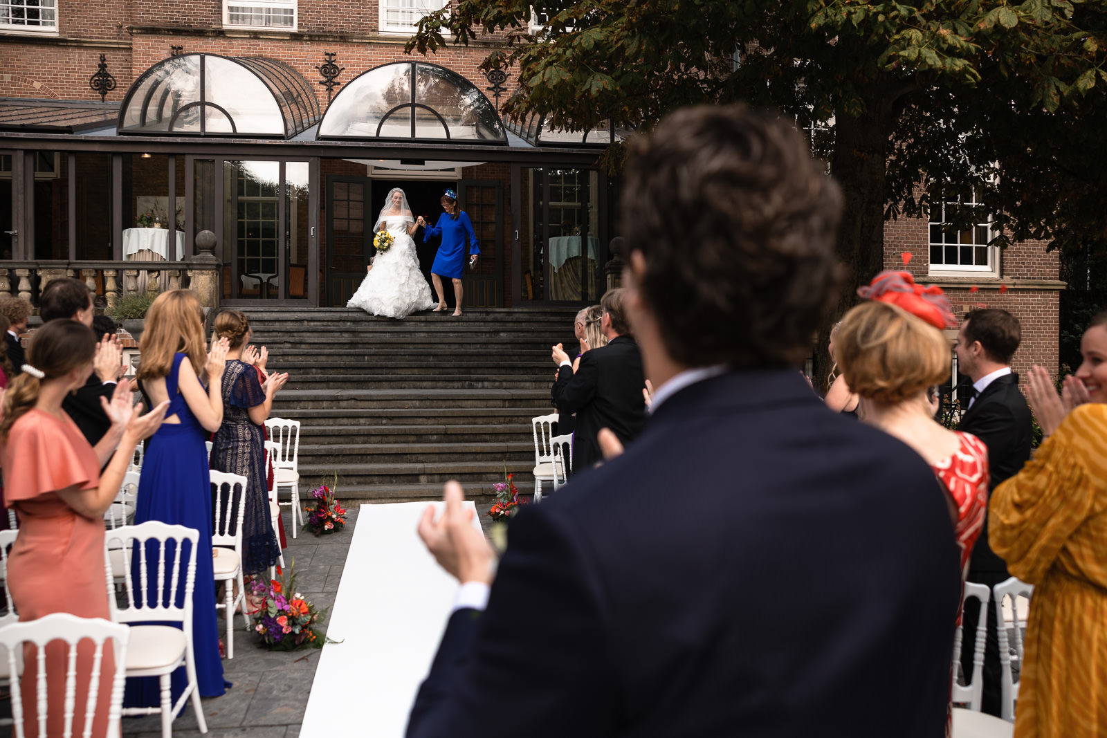 Bruid komt met moeder de trap af voor de buitenceremonie bij kasteel de Wittenburg in Wassenaar