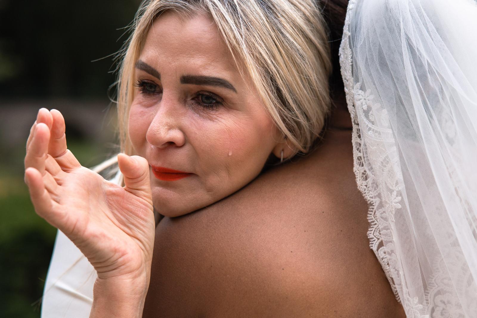 Close-up van een ontroerde gast die een traan wegpinkt tijdens de omhelzing op de bruiloft.