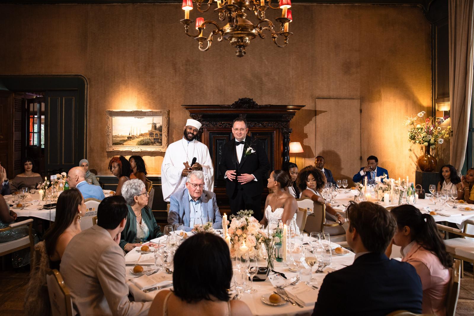 Bruidegom Ronald en de priester spreken de gasten toe tijdens het sfeervolle diner in de kasteelzaal.