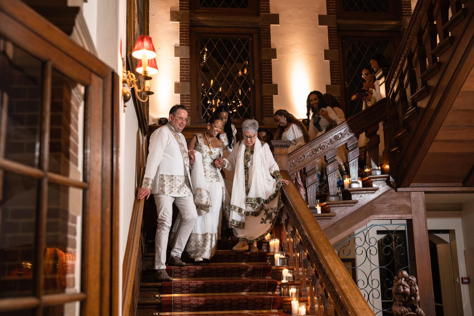 Het bruidspaar en gasten in traditionele Ethiopische kleding dalen de kasteeltrap af naar het feest.