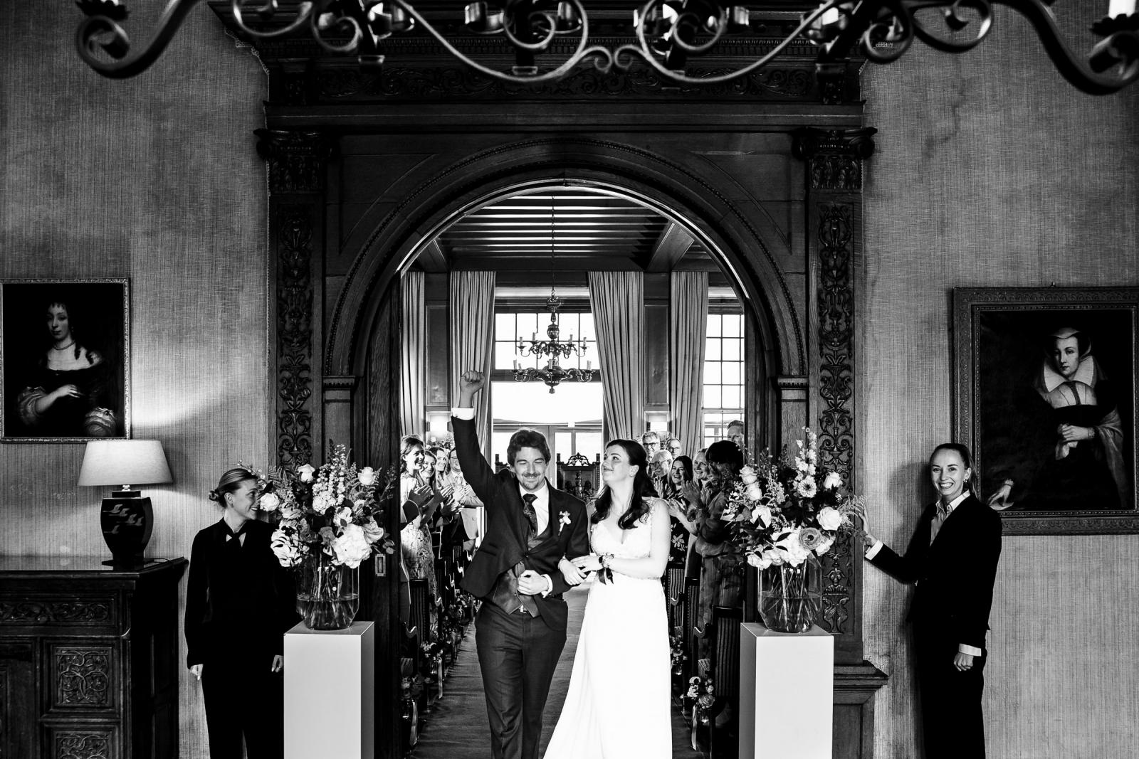 Zwart-wit uitloop ceremonie, bruidspaar juichend door bloemen in Kasteel de Wittenburg
