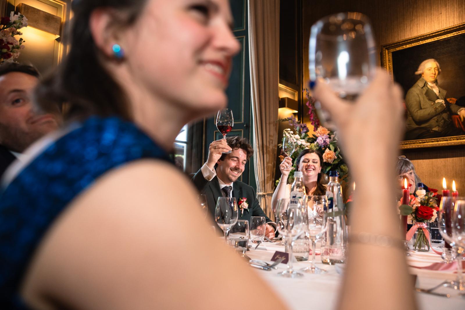 Proostmoment aan tafel met bruidspaar op achtergrond, diner bruiloft Kasteel de Wittenburg