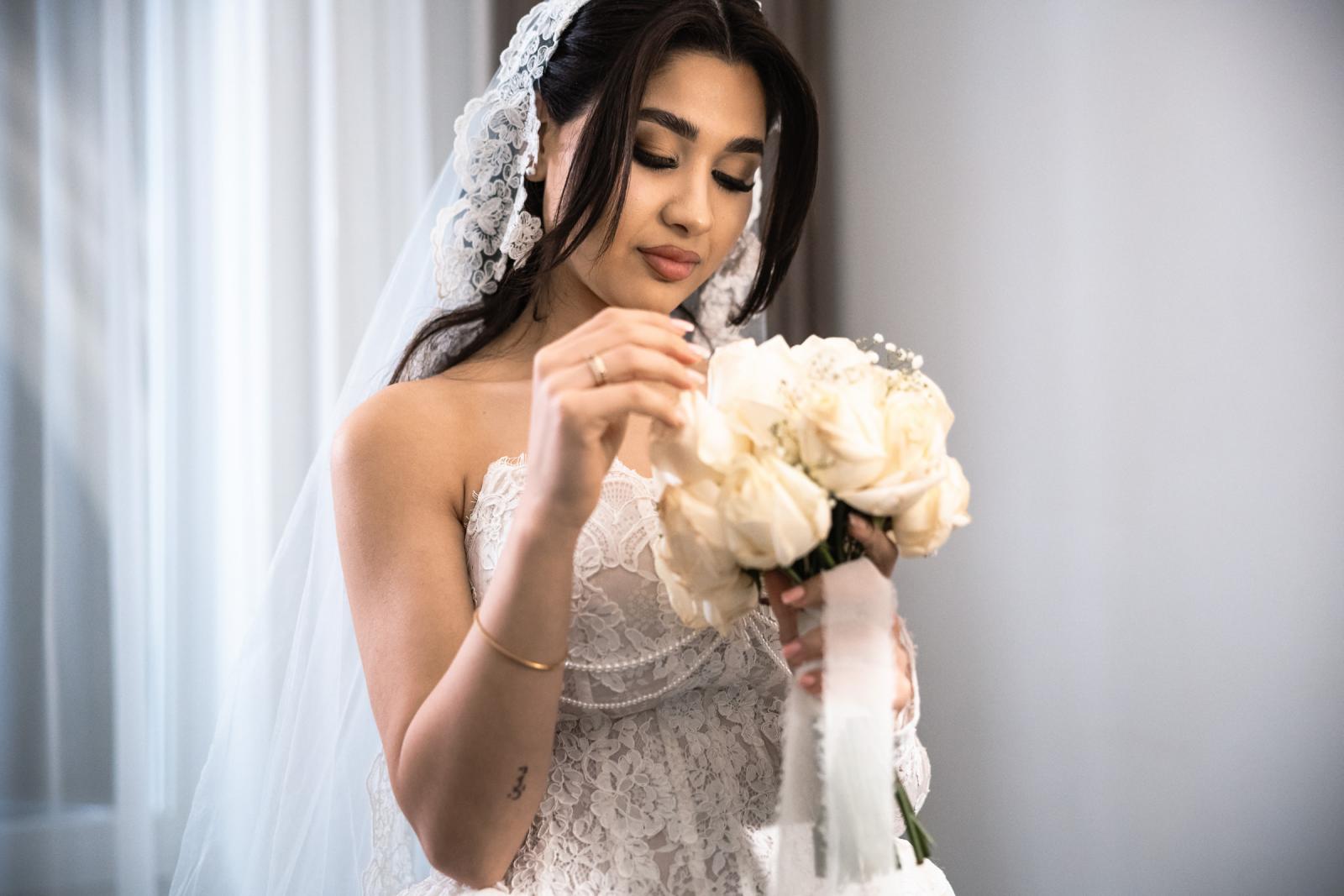 Bride adjusting her bouquet of cream roses, lace veil framing her face
