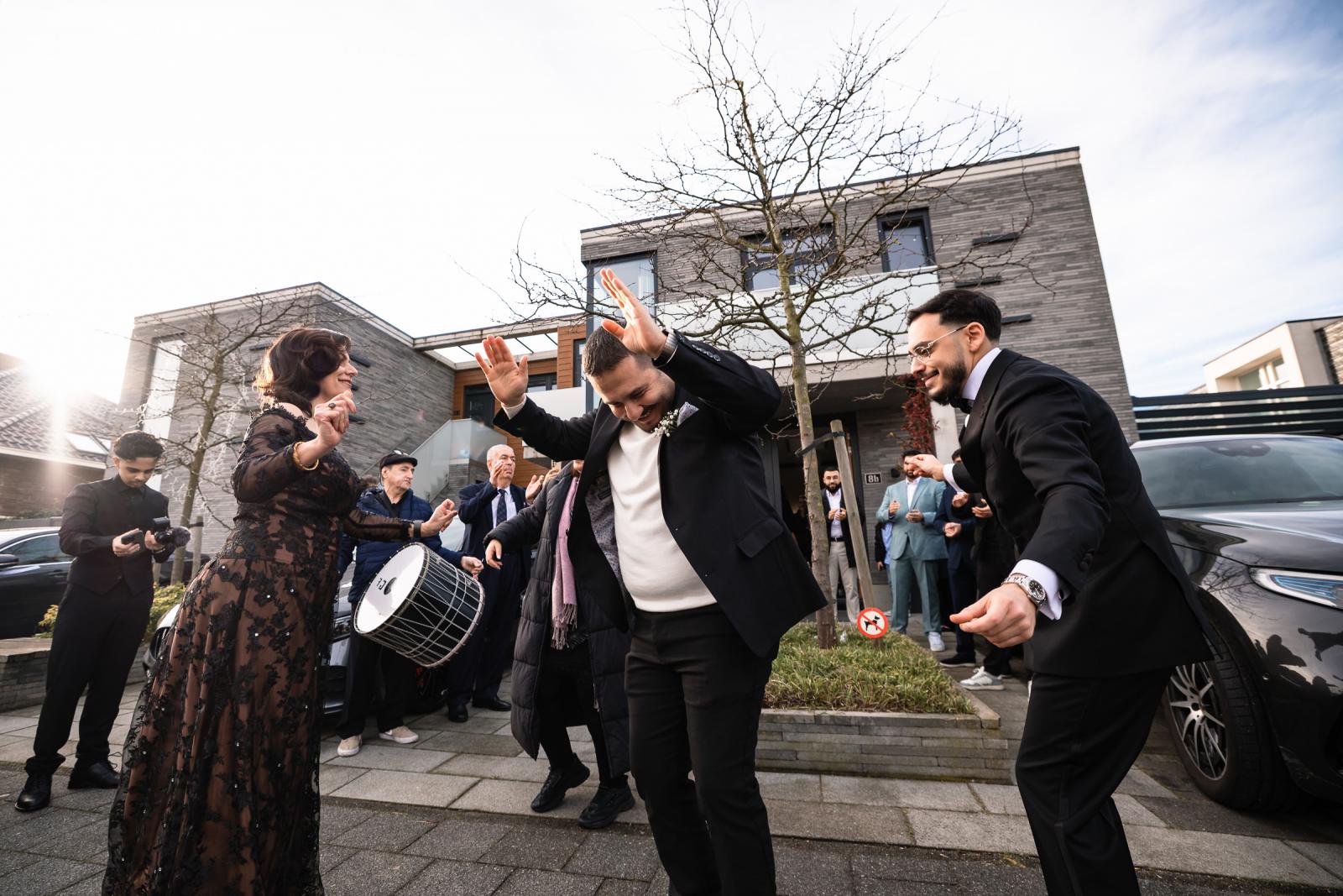 Groom and family dancing outside, joyful street moment with musicians