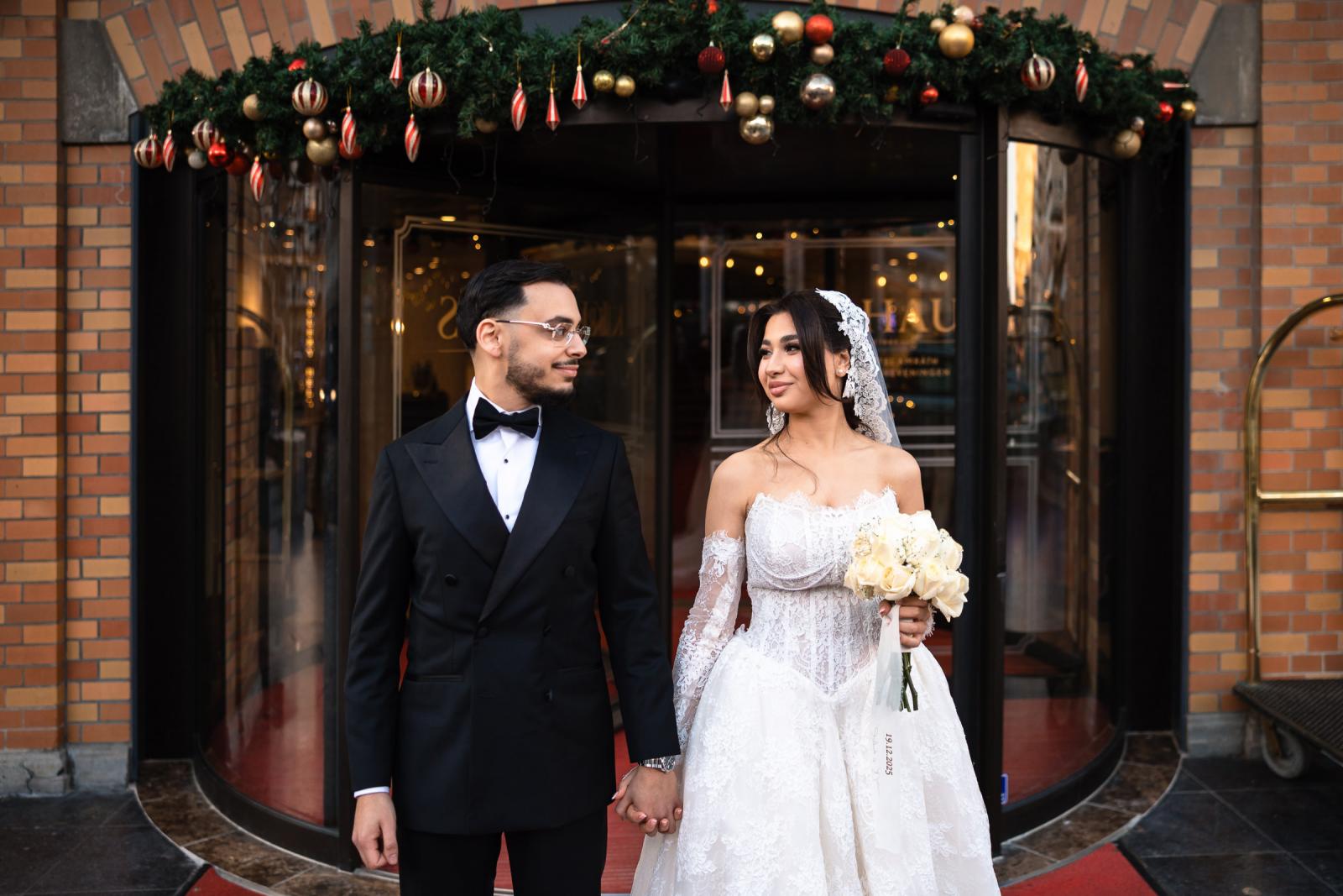 Bride and groom smiling at each other in front of the Kurhaus, festive garland above