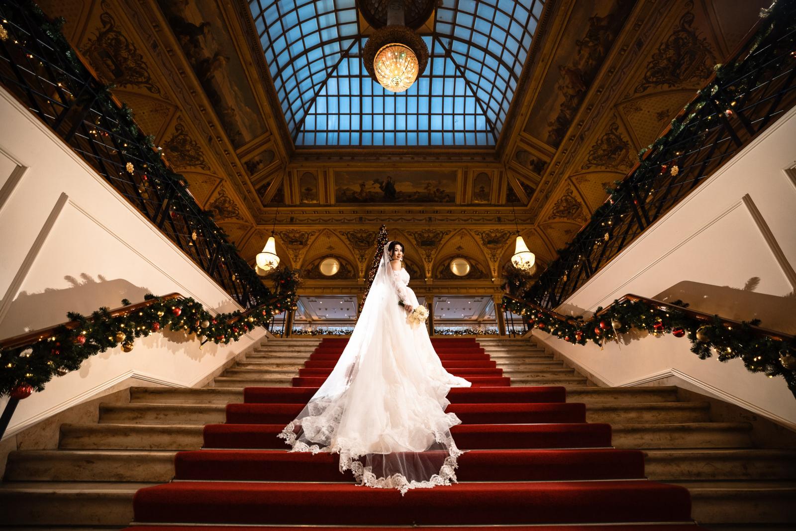 Bride posing alone on the grand red staircase of the Kurhaus, Christmas lights above