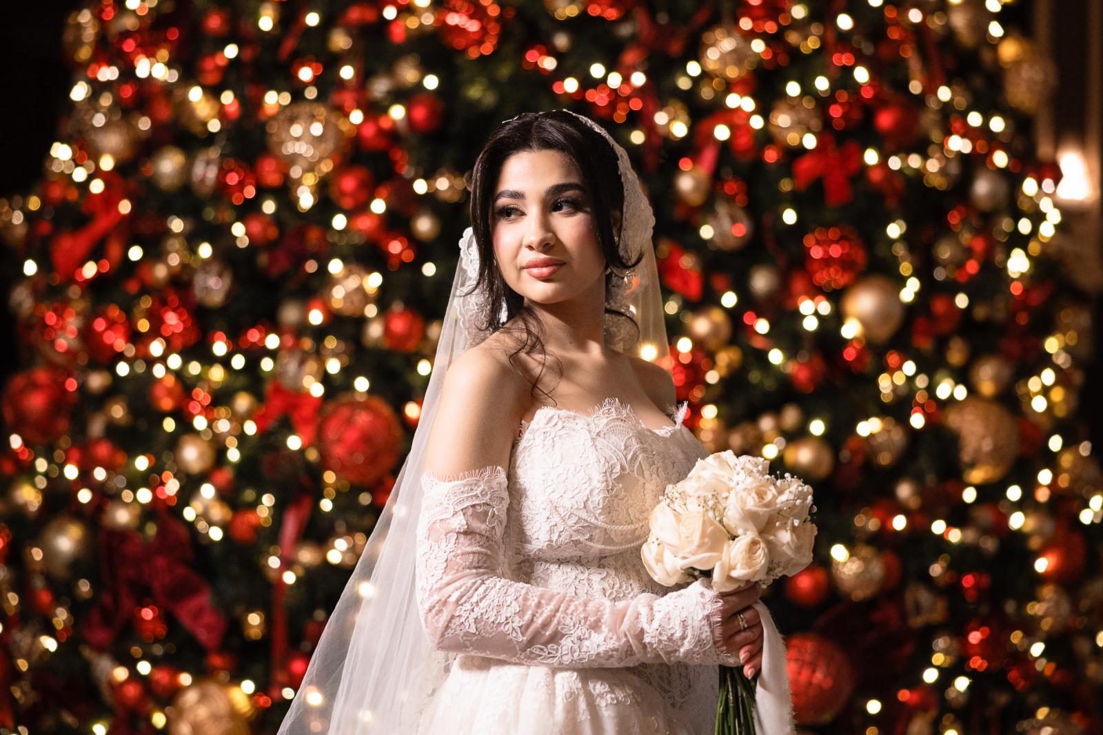 Bride posing in front of a sparkling Christmas tree, holding her bouquet