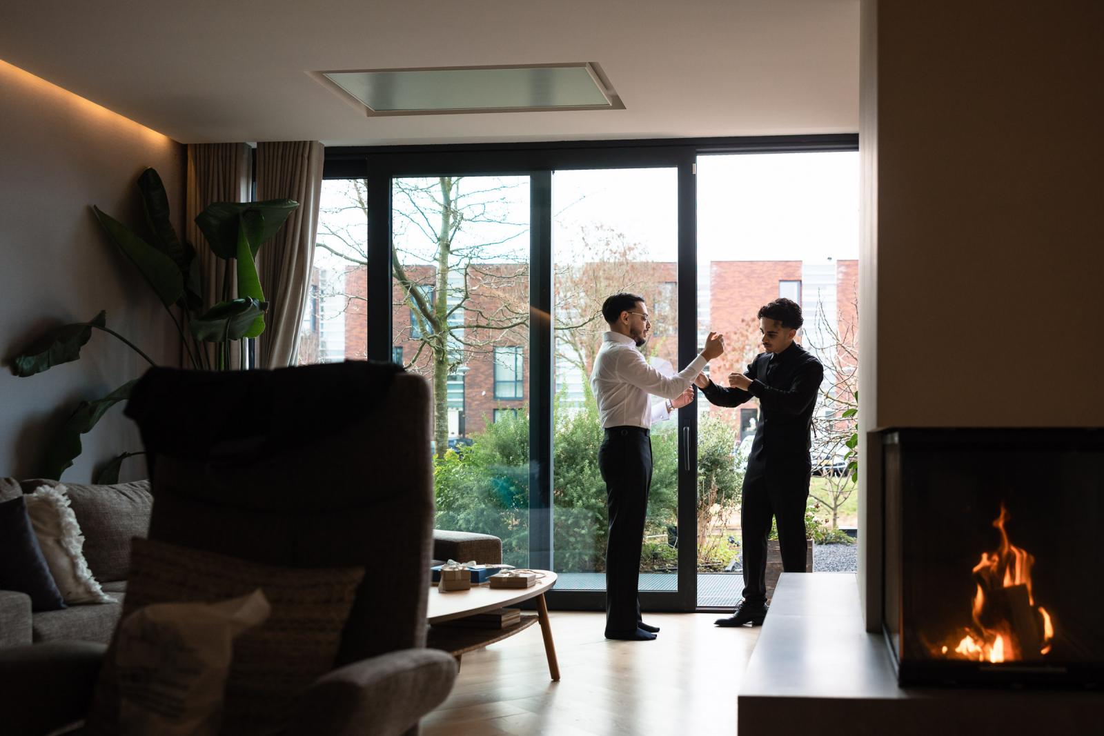 Groom getting ready at home with a family member, natural light in modern living room