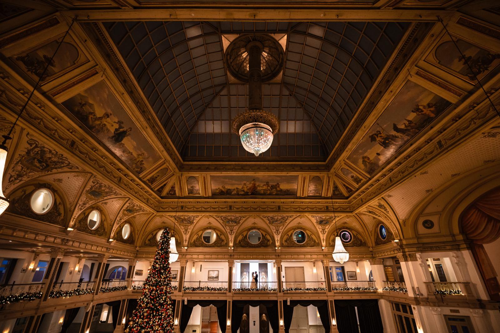Wide shot of the Kurhaus ballroom with couple on balcony, ornate ceiling and chandelier
