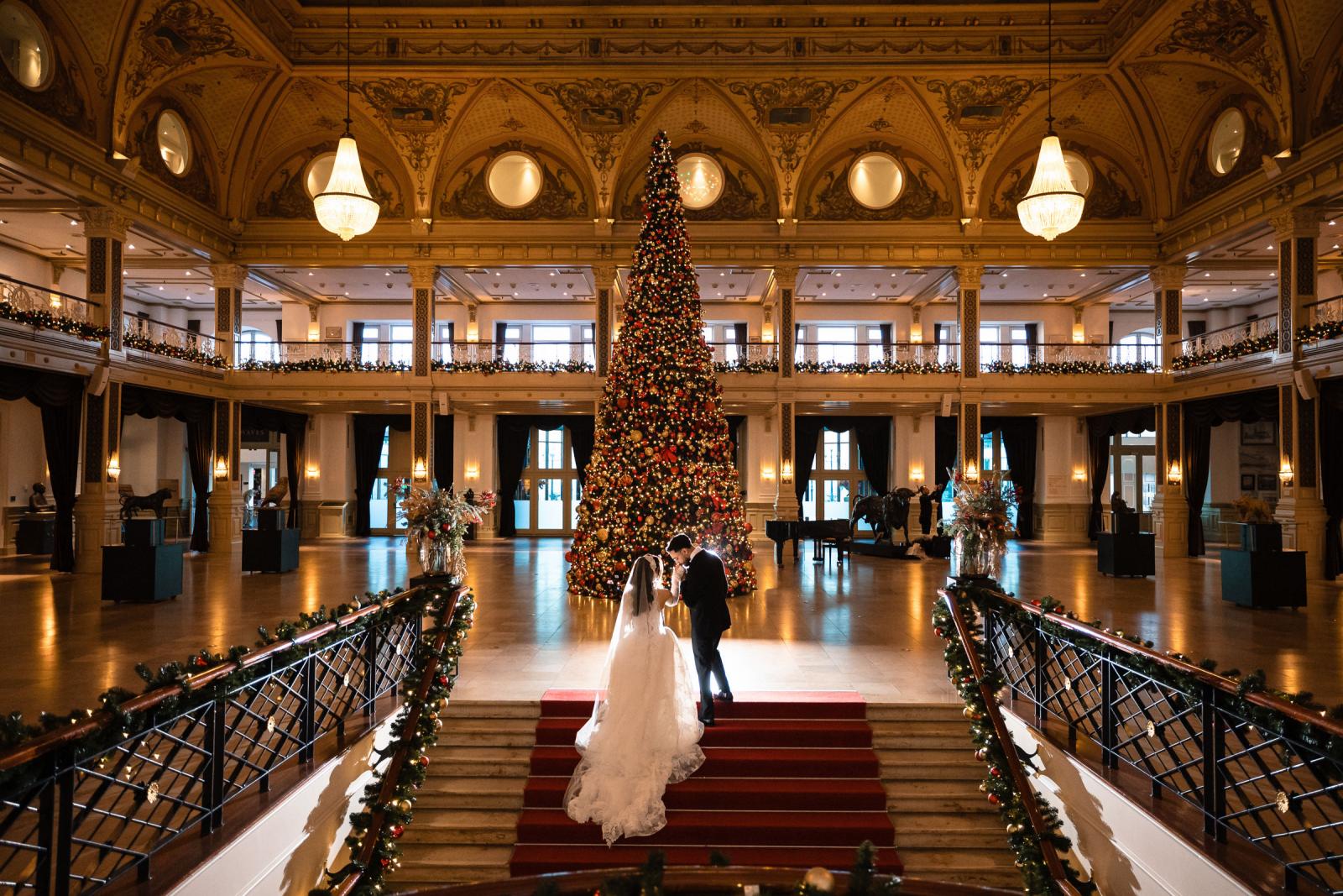 Bride and groom walking up the stairs towards the grand Christmas tree in the Kurhaus