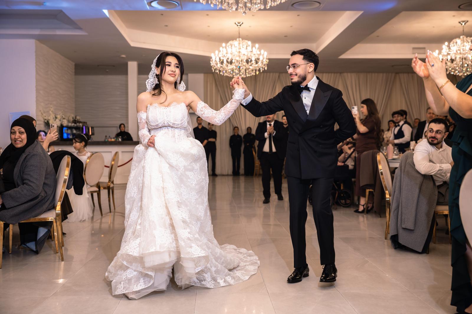 The bride and groom making their entrance at the reception, holding hands and smiling as guests applaud.
