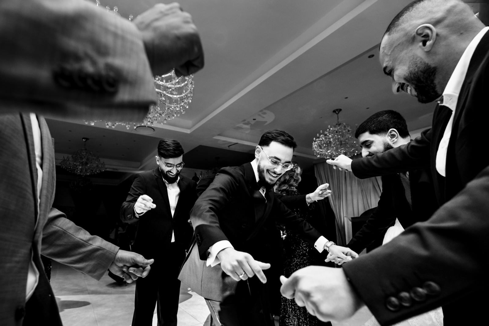 The groom dancing in a circle with friends and family, everyone smiling and celebrating.