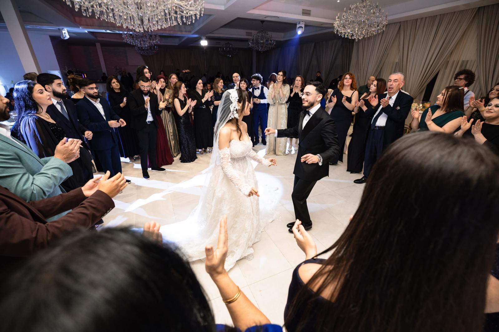 The bride and groom dancing together, surrounded by clapping guests on the dance floor.