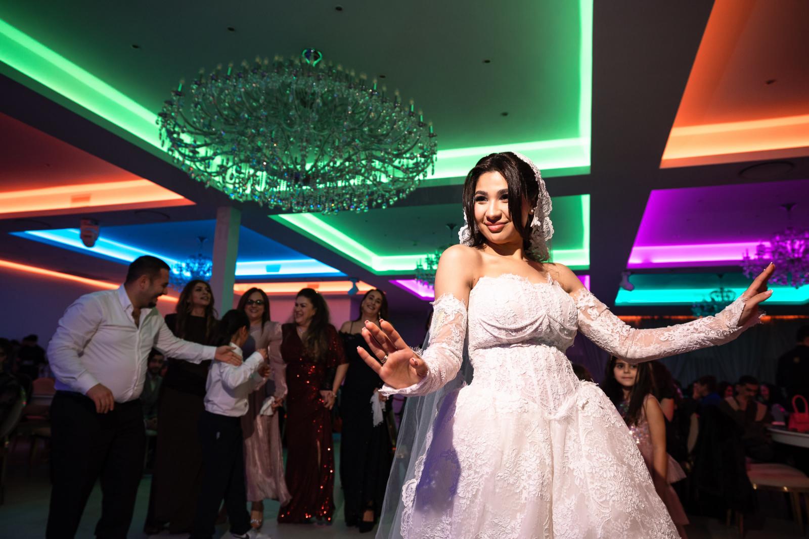 The bride dancing at the reception, illuminated by colorful neon lights and surrounded by smiling guests.