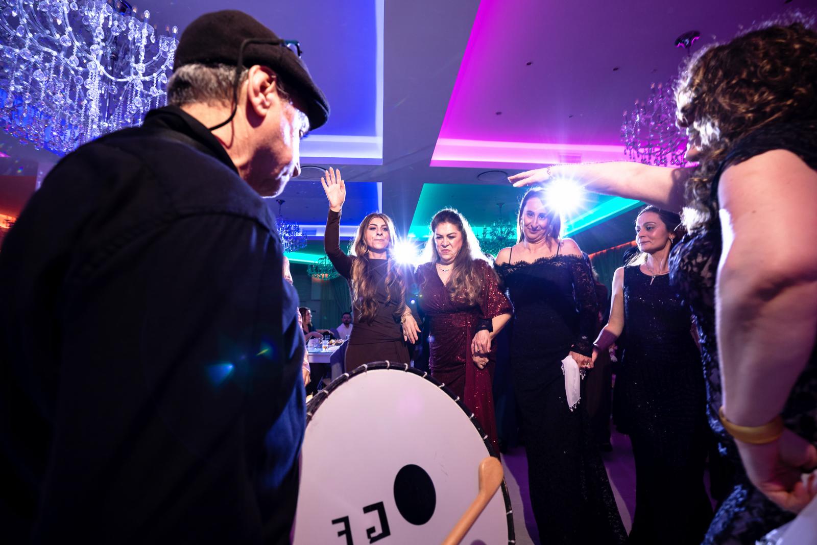 Female guests dancing in a circle around a drummer, with vibrant lighting and festive energy.