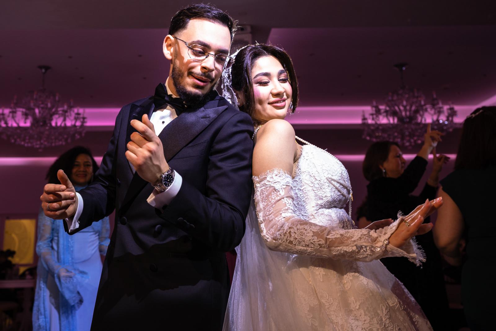 The bride and groom dancing back-to-back, smiling under the pink-lit reception hall.
