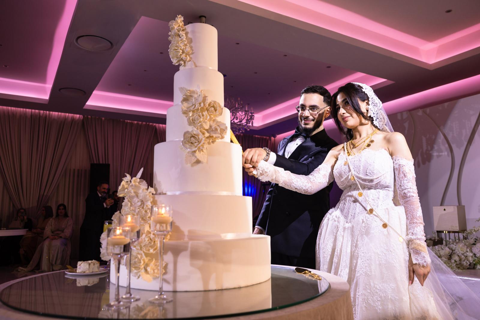The bride and groom cutting a tall, elegant wedding cake adorned with white flowers.
