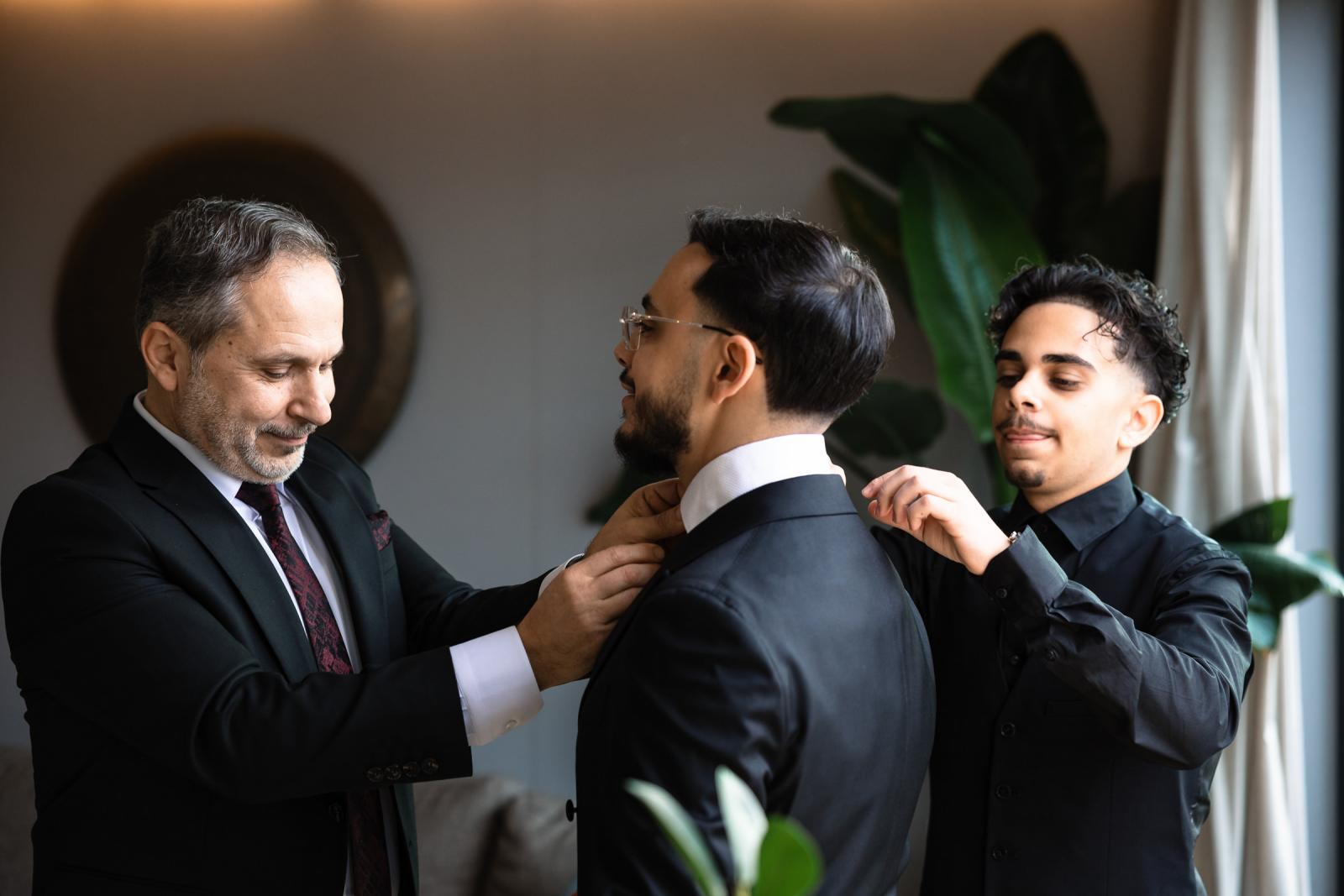 Close-up of groom’s collar being adjusted by his father and brother