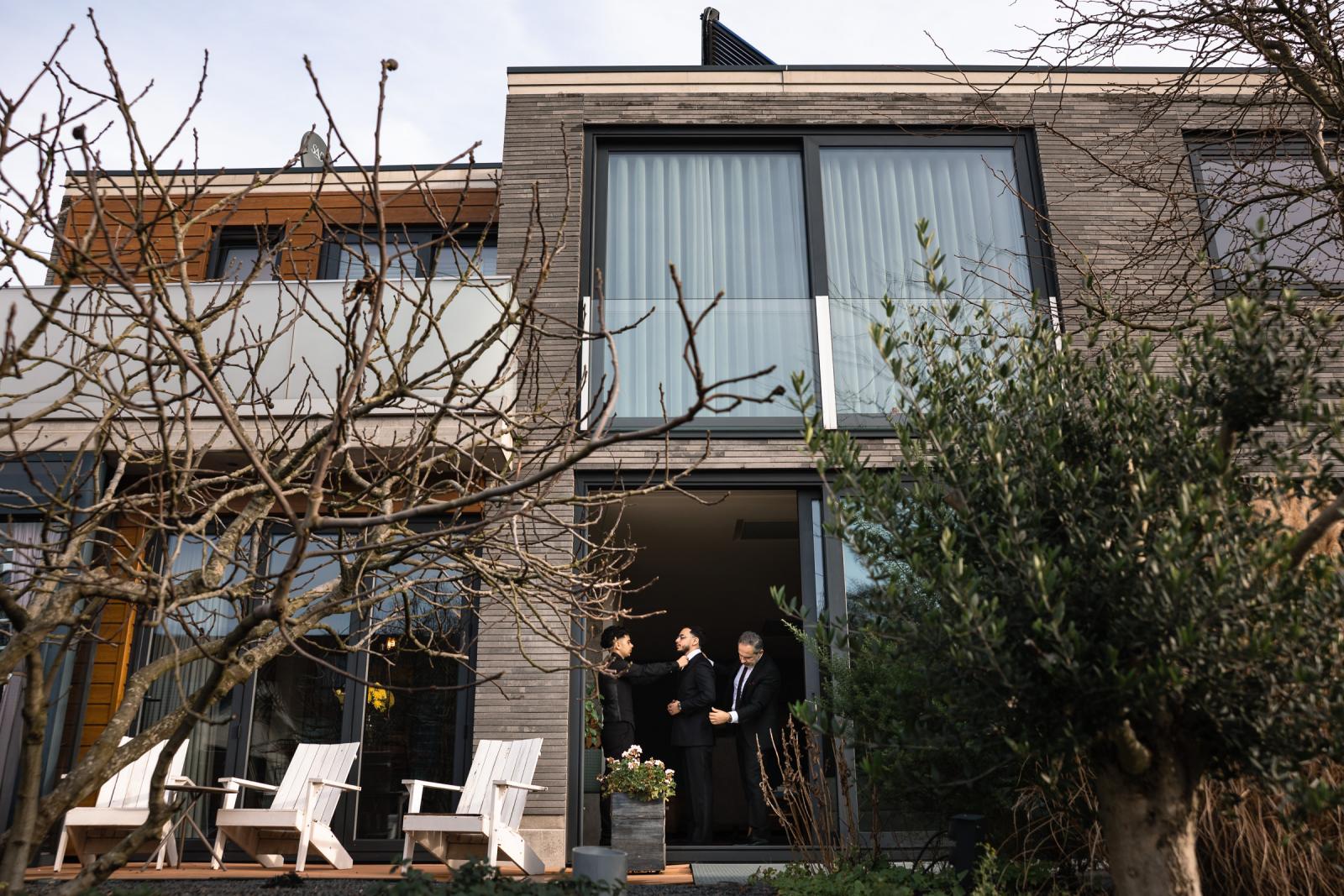 Groom, father, and brother preparing at home, seen from the garden through open doors